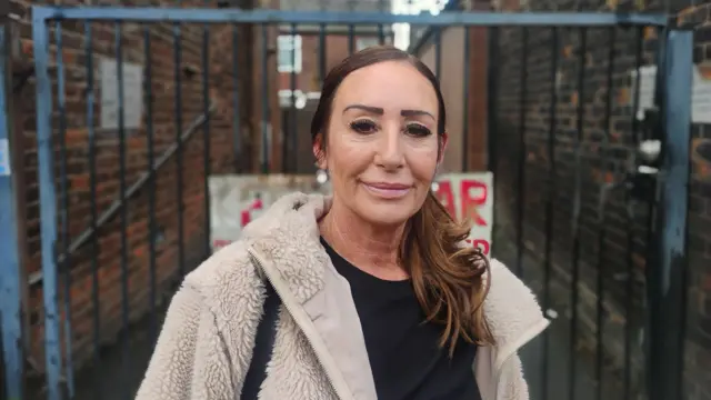Julie Doherty stands in front of a gate and looks towards the camera