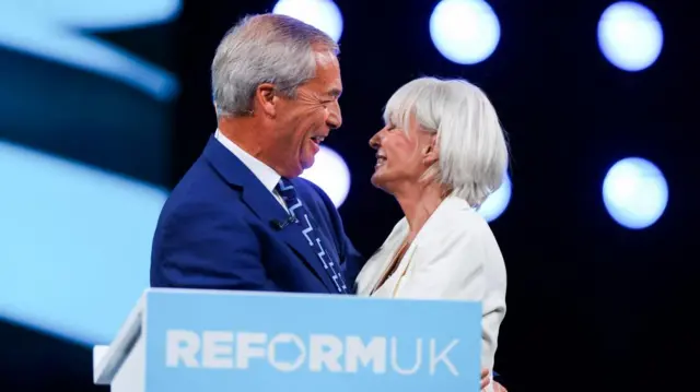 Nigel Farage and Nadine Dorries hug behind a Reform UK podium