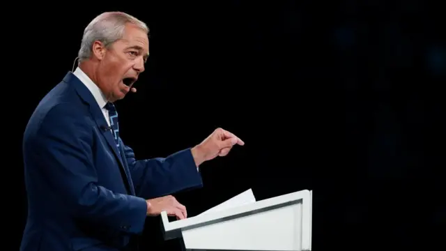 Farage speaks and wears a suit behind a podium.