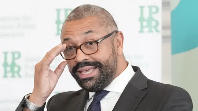 Headshot of James Cleverly as he fixes his glasses and is mid-speaking