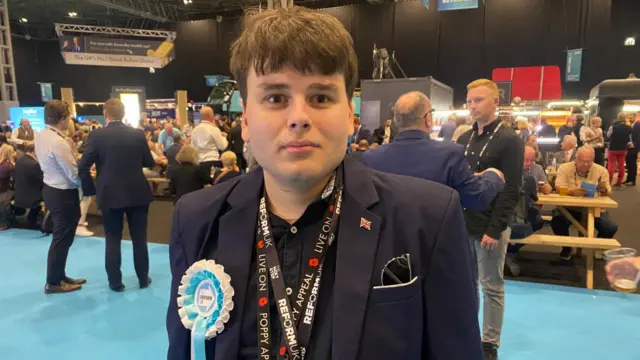 A man in a dark blue blazer with a Reform UK rosette attached to it
