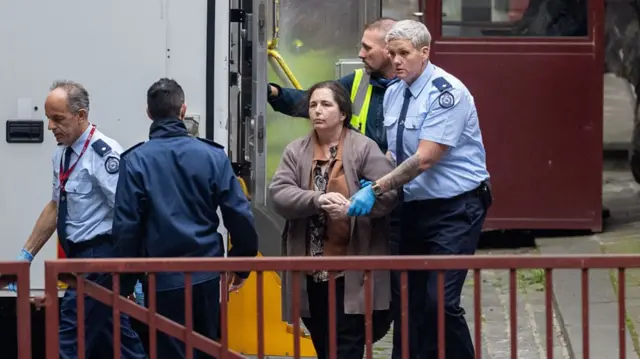 Authorities wearing blue uniforms walk beside Australian murder convict Erin Patterson