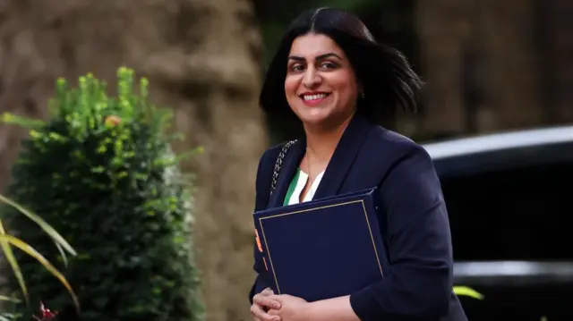 Shabana Mahmood grips a binder and smiles as she arrives at Downing Street