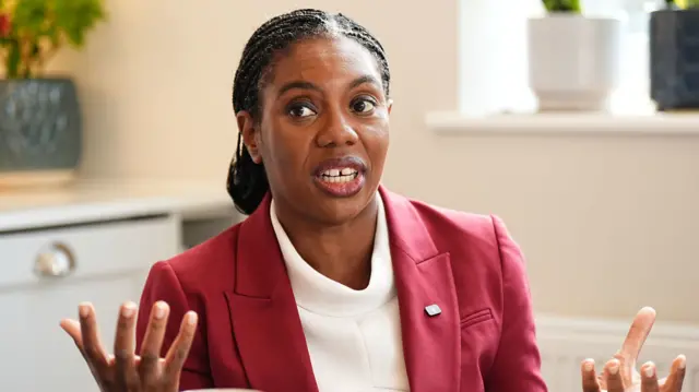 Tory leader Kemi Badenoch, wearing a red suit, gestures with her hands as she speaks