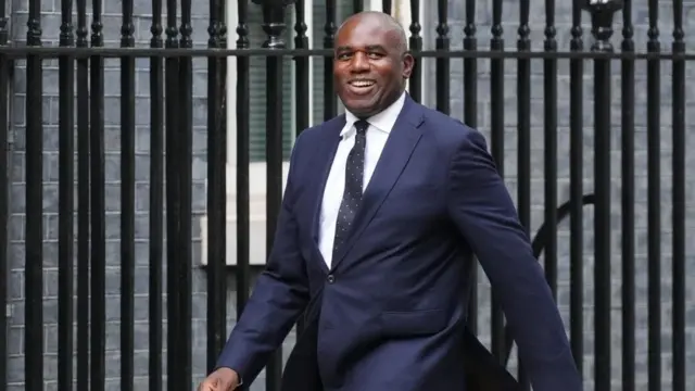 A smiling David Lammy walks in a suit down Downing Street