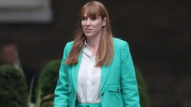 Angela Rayner, wearing a bright green suit, walks towards 10 Downing Street