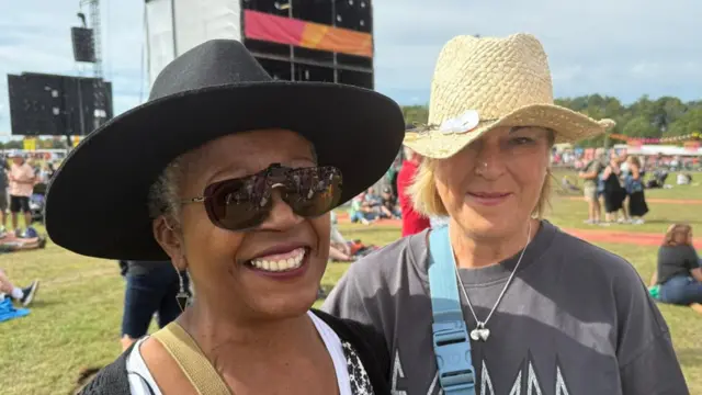 Tiggy and Jax are both wearing cowboy hats and smiling. They are standing in a busy field at the festival.
