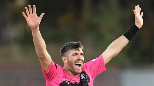 Somerset bowler Craig Overton with his arms aloft after taking the wicket of Rob Yates