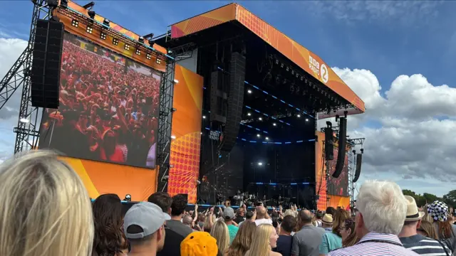 A packed crowd looking towards the large orange main stage.