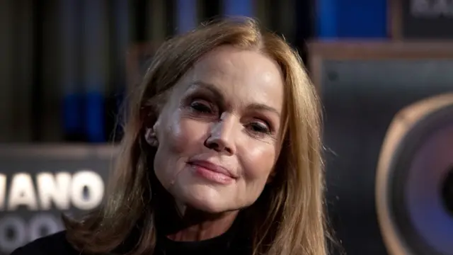 Belinda Carlisle smiles at the camera. She has shoulder length light brown hair and wears a black top.