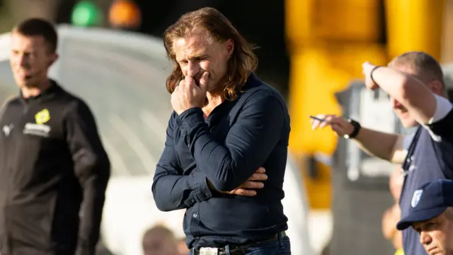 Gareth Ainsworth holds his hands over his mouth with his eyes closed while standing on the touchline