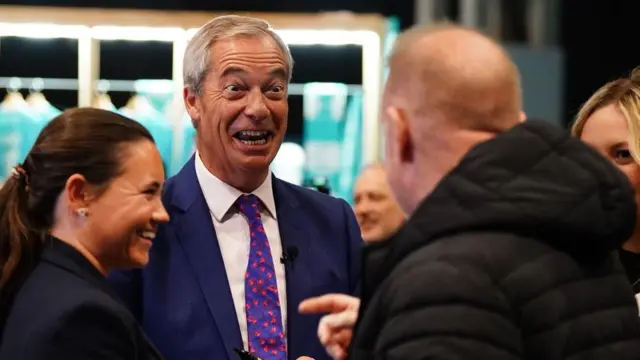 Nigel Farage makes a face while speaking to someone at the Reform UK conference in Birmingham.