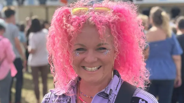 Michelle Steward has bright pink curly hair with sunglasses on top.
