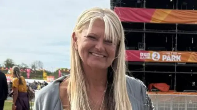 Marie Atkinson has long blonde hair and is standing in front of a large BBC Radio 2 banner. Behind her are people queuing to get in.