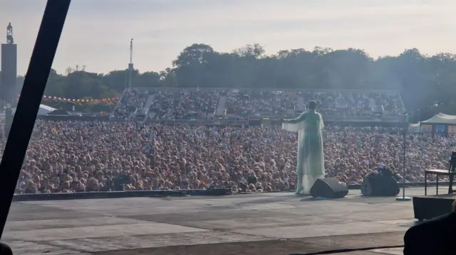 Jessie J singing on stage. The picture is taking from backstage. Hundreds of people watch her from below the stage.