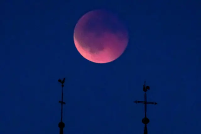 The blood moon rises behind the cross and rooster of two churches' steeples during a total lunar eclipse in Bottens, Switzerland, 07 September 2025.