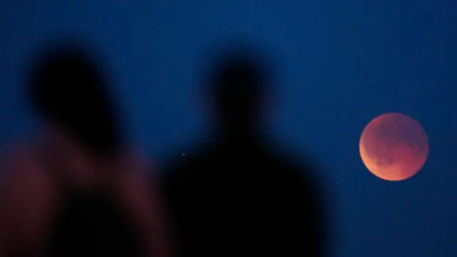 Two people look at the blood moon, they are seen only from behind and are out of focus