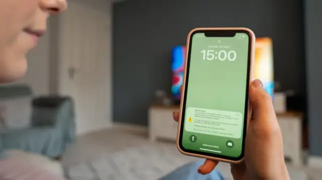 A person holding up a mobile phone displaying an emergency test alert