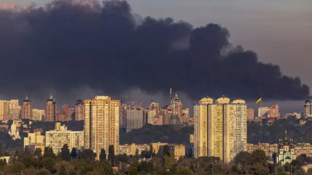 A view of the city of Kyiv and the high rise buildings. Dark smoke billows out from behind the tall buildings.