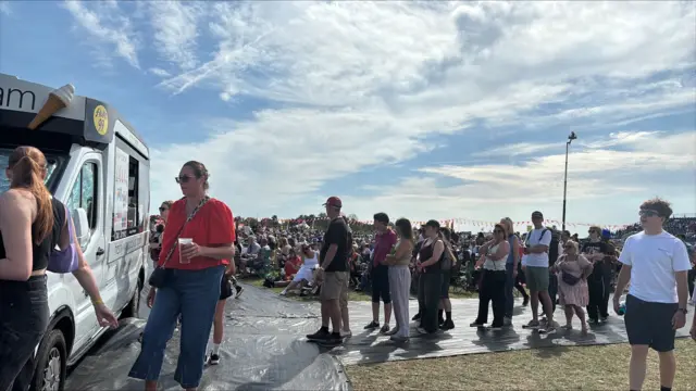 A queue of people waiting in front of an ice cream truck during a festival.