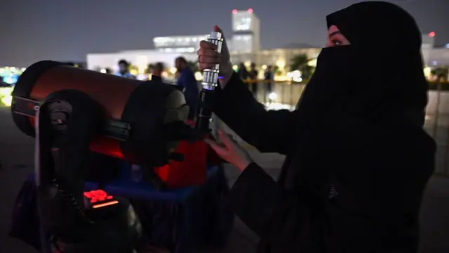 A woman in a Niqab uses what appears to be a very expensive telescope or piece of camera equipment