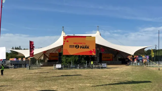 A large marquee covers a stage and area for the crowd. A big screen is projecting "welcome to BBC Radio 2 in the Park" with an orange background.