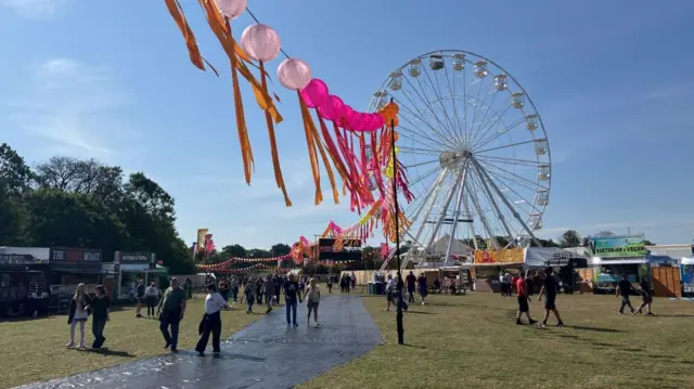 People milling around an area away from the stage. There are food trucks, colourful lanterns and a Ferris wheel.