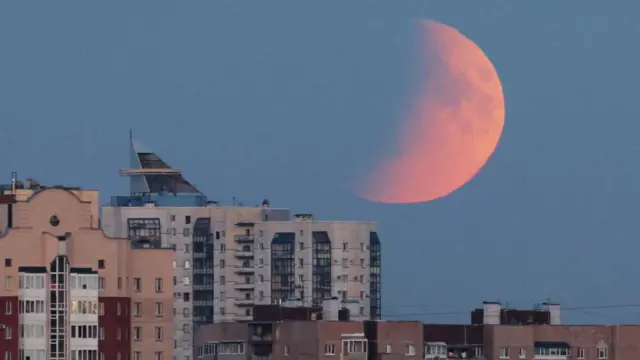 Half of the red moon seen over blocks of flats