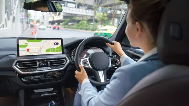 A woman wearing a light blue shirt is driving a car.