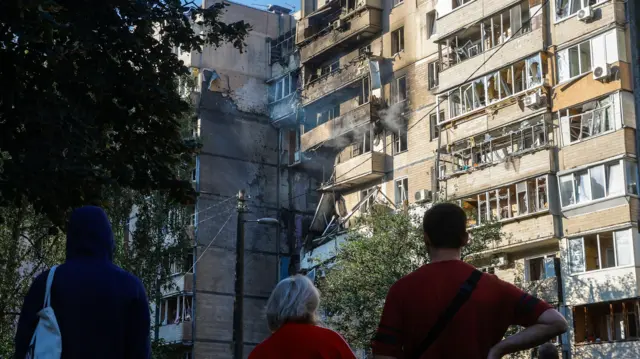 Local residents look up at apartment block in Kyiv that is smouldering after a Russian hit overnight