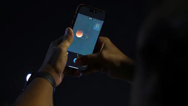 A person taking a photo of the Moon on their phone