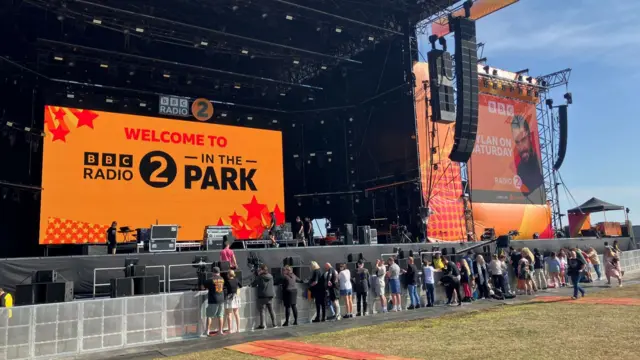 A small crowd of people standing right in front of the large orange main stage.