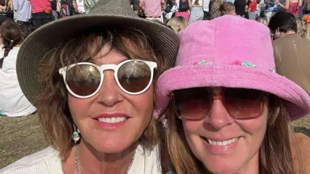 Two women with short brown hair wearing bucket hats and sunglasses take a selfie image and smile.