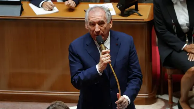 French Prime Minister Francois Bayrou gives a speech holding a microphone in the National Assembly.