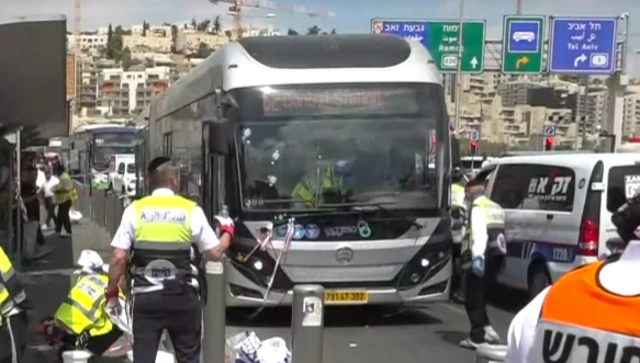 A parked bus with three bullet holes in the windscreen and emergency workers stood around