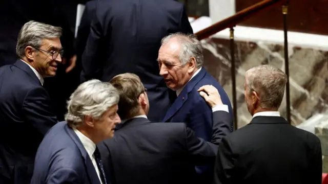 French Prime Minister Francois Bayrou wearing a suit surrounded by lawmakers.