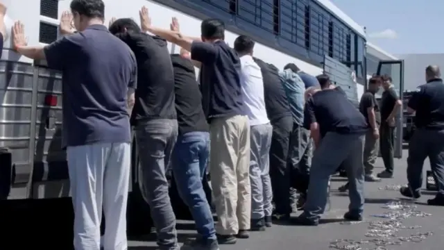 Workers lined up with their hands against a bus outside the factory
