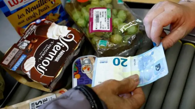 A woman hands over a €20 note in a supermarket