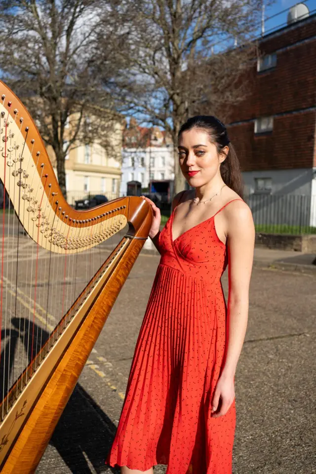 A girl in a red dress holds a harp.