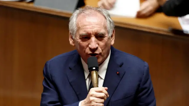 Prime Minister Francois Bayrou speaks into a microphone, wearing a suit, in the French Assembly.