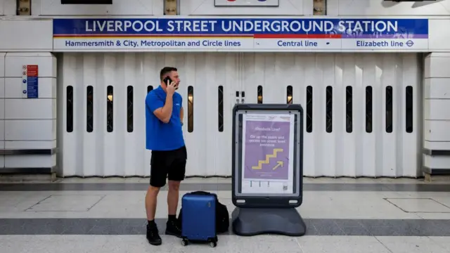 A commuter outside the closed Liverpool Street tube station looks to the side, speaking on the phone.