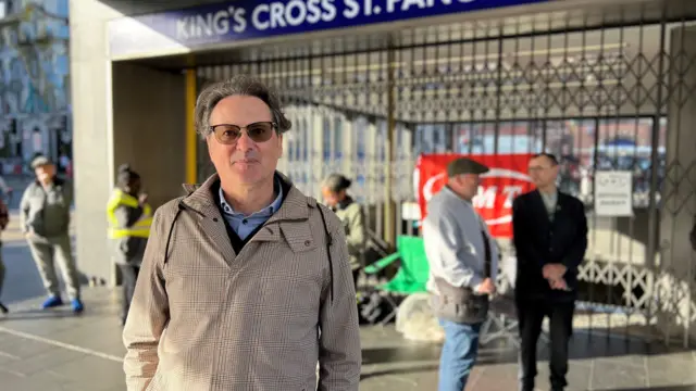 Jared Wood in a checked raincoat and glasses outside the shuttered Tube station
