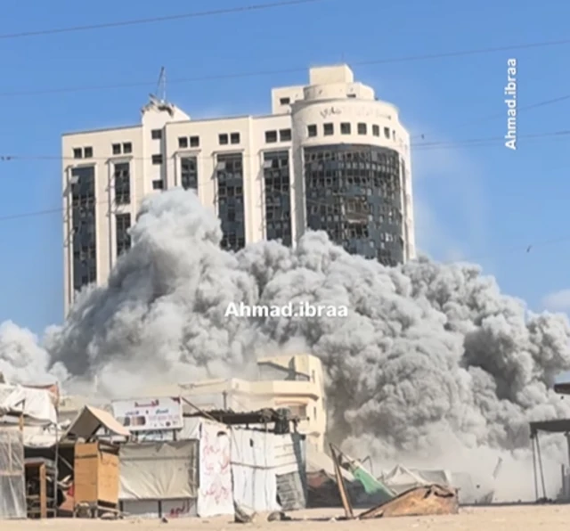 A large plume of smoke erupts from the base of a high-rise building