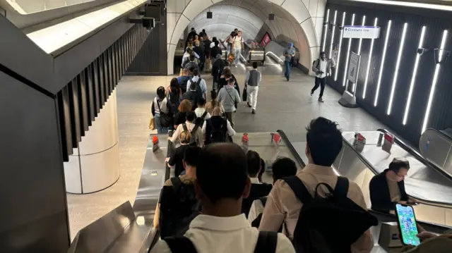 A large crowd of people travelling down escalators at Bond Street station.