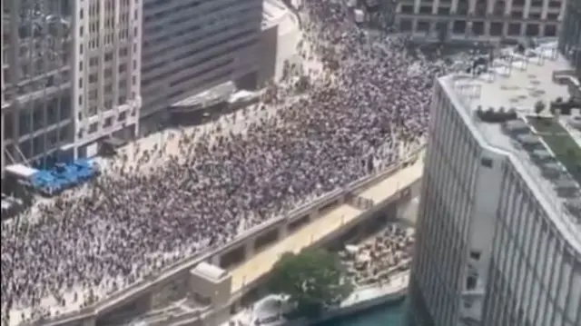 A very large crowd of people walking along a road as viewed from the top of a nearby building