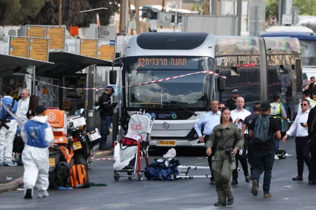 Bus with police tape and emergency workers standing around. Some people are wearing white forensics outfits.