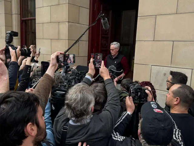 Reporters crowd around Ian Wilkinson as he speaks outside court