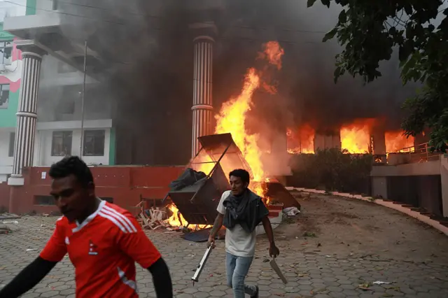 Two Nepali protesters  walk past flames outside the burning Nepali Congress Party