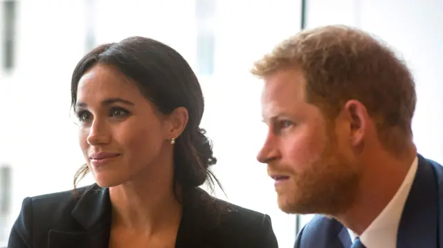 Megan Markle, dressed in black next to Prince Harry, in a dark suit