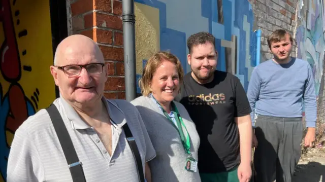 Three men stood either side of a woman wearing a grey jumper